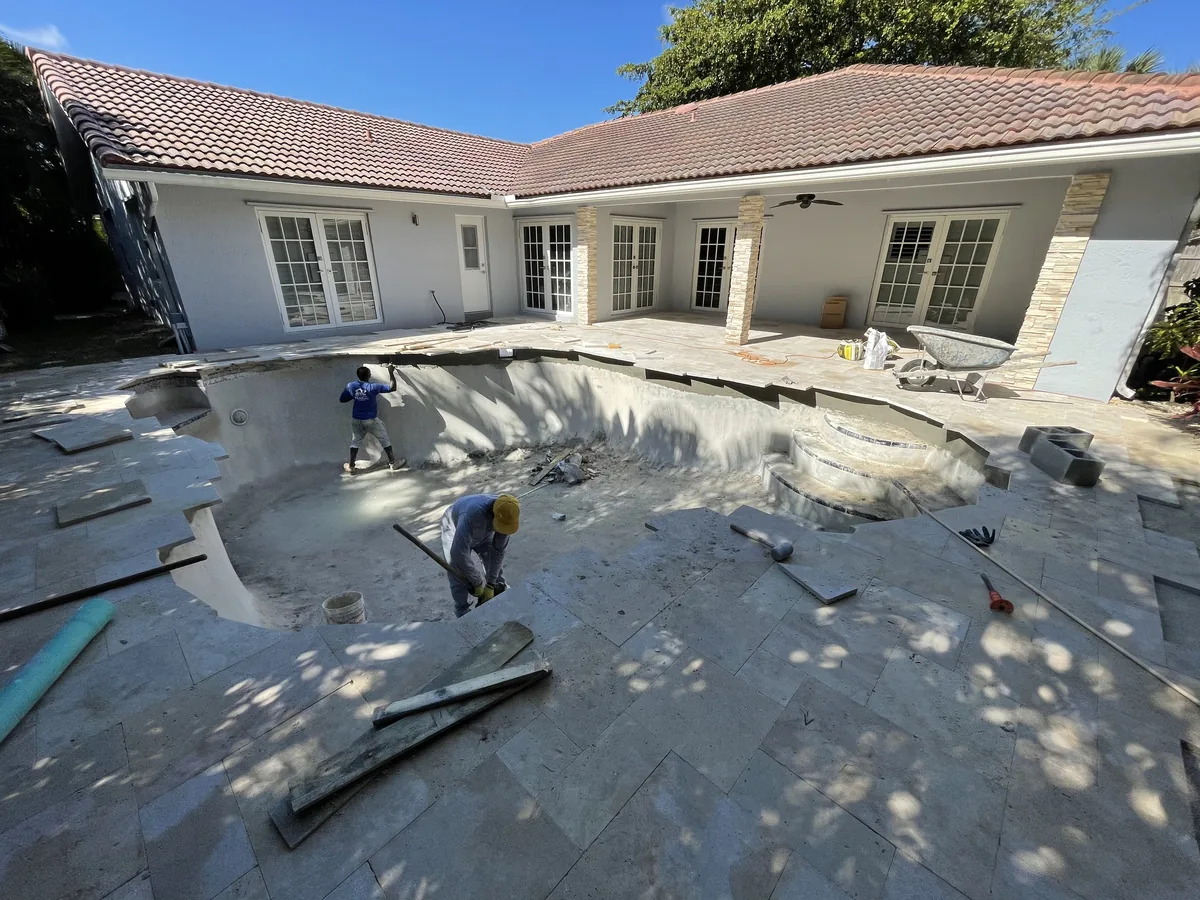Crew setting new ivory travertine around a drained freeform pool