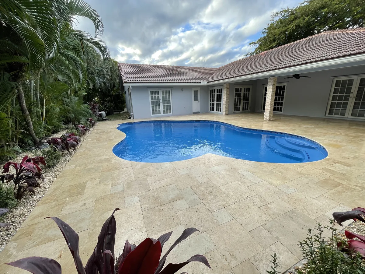 Wide view of a finished freeform pool and travertine deck behind a single-story home