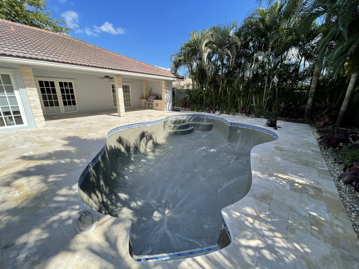 Freeform pool shell prepped for new finish, with the new travertine deck already laid around it