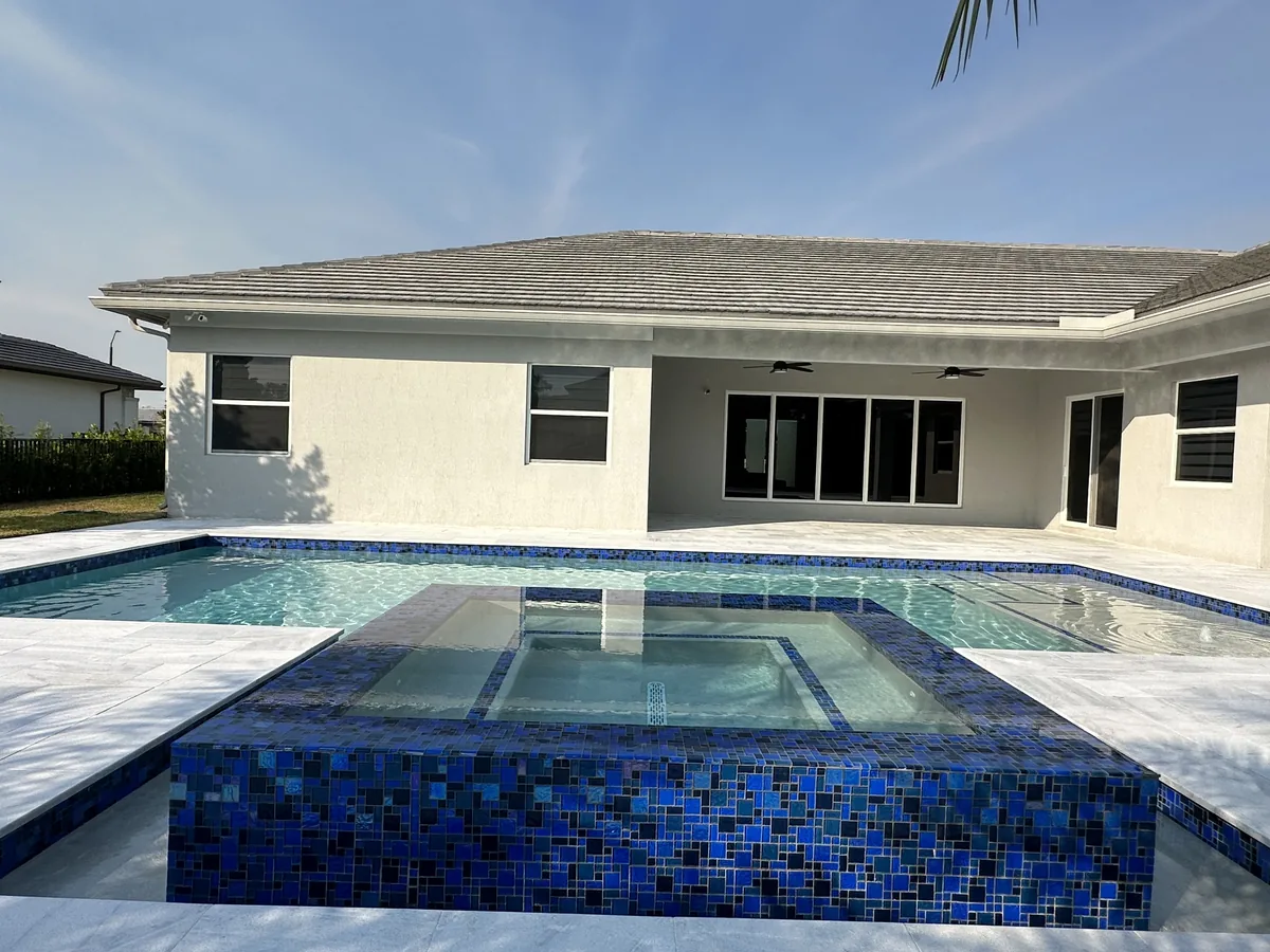 Raised spa clad in deep blue glass mosaic tile beside a pool and pale stone deck