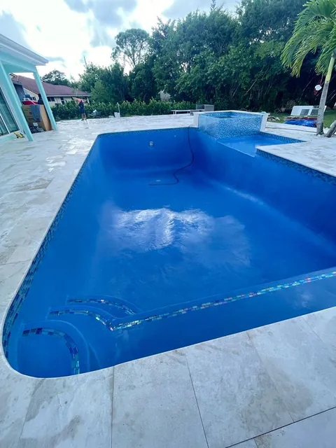 Pool filling with water after a new blue finish, with a travertine deck and glass tile accents
