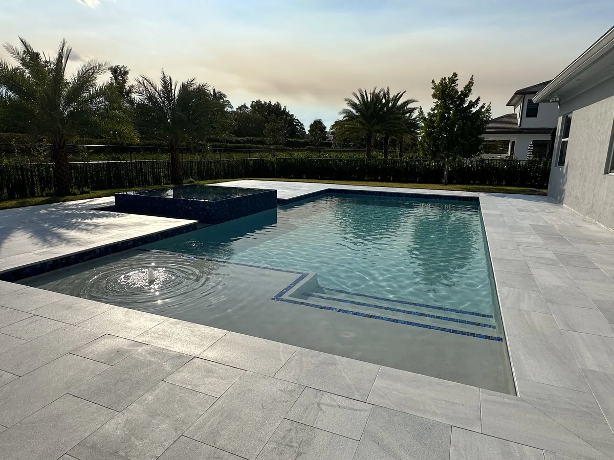 Pool with a tile-edged sun shelf, raised spa and pale stone deck
