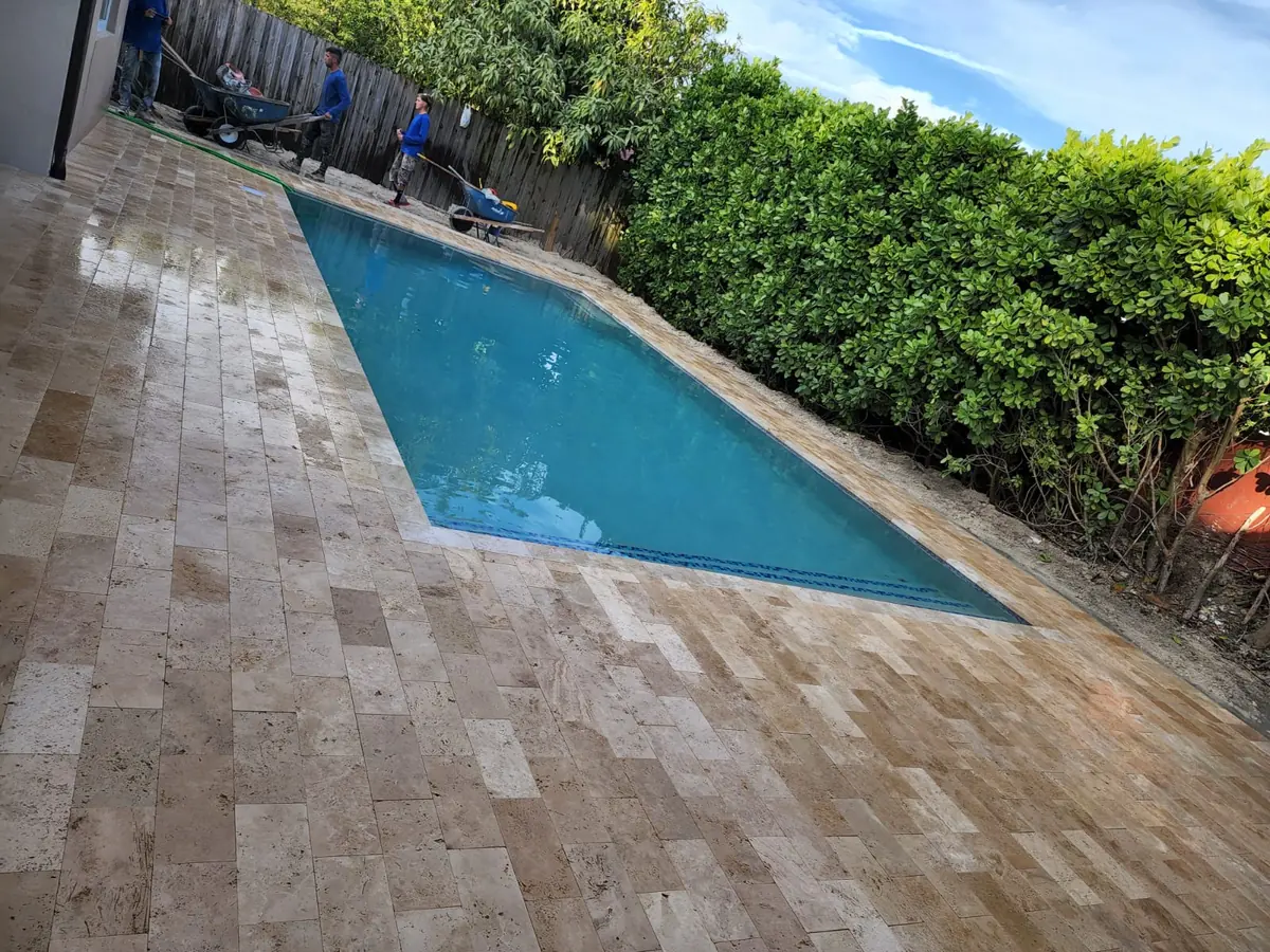 Travertine deck running the length of a narrow pool beside a tall hedge