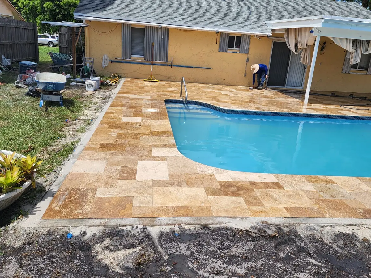 Golden travertine pavers laid around a kidney-shaped pool behind a stucco home