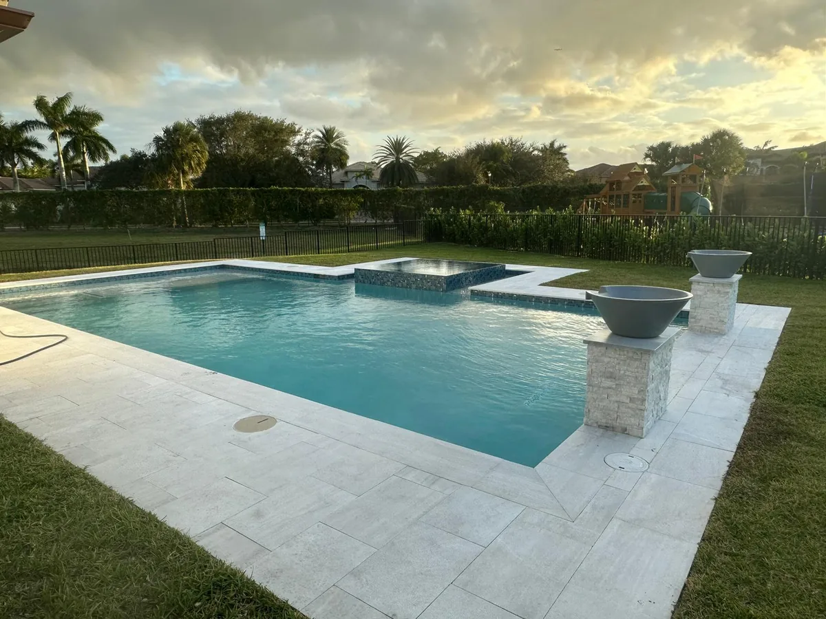 Pool with a white paver deck, raised spa and fire bowls at dusk